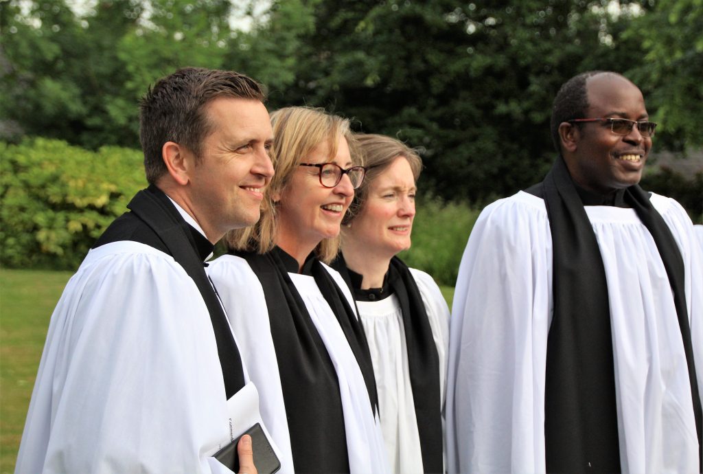 Four people in vicars' vestements in a garden looking at a camera